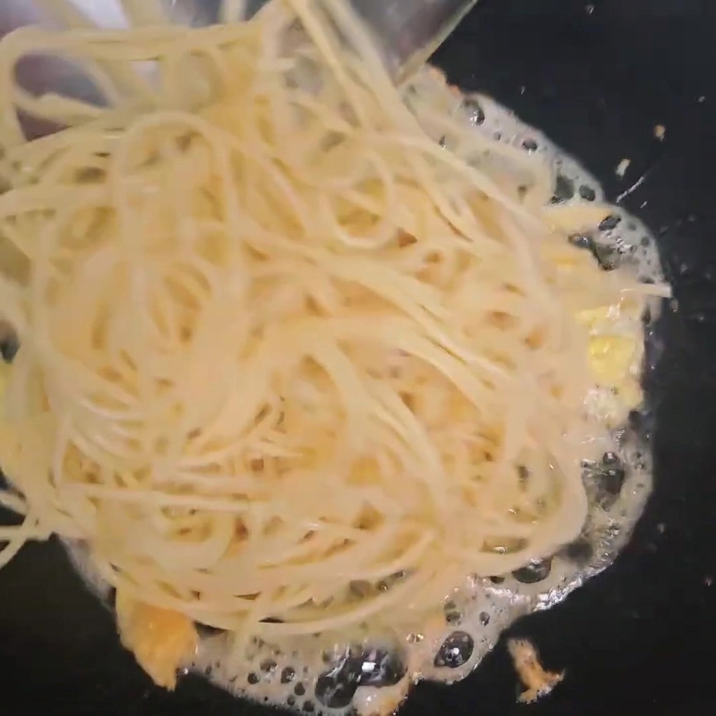 Ugotowane spaghetti dodawane do patelni z usmażonymi jajkami.