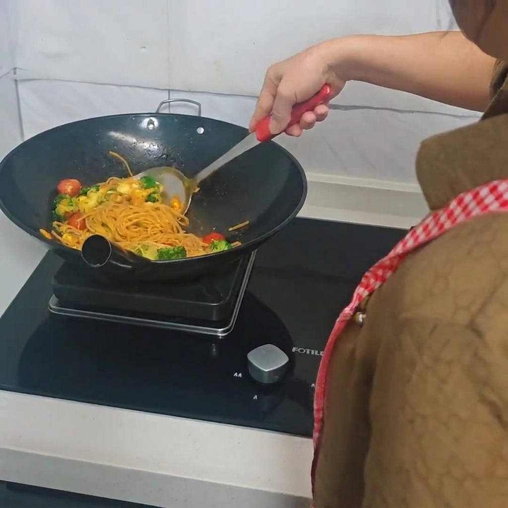 Osoba używająca łopatki do mieszania spaghetti, brokułów, pomidorów i jajek na patelni.