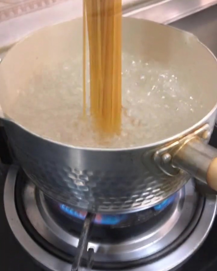 Surowe spaghetti zanurzane w gotującej się wodzie w garnku.
