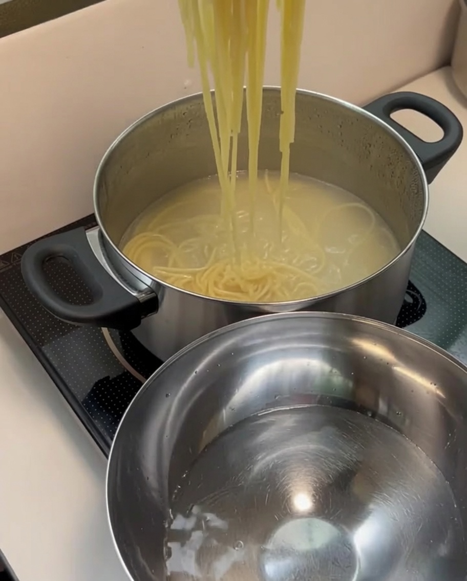Odcedzony makaron spaghetti przekładany do stalowej miski z czystą, zimną wodą.