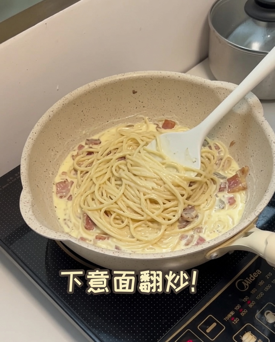 Ugotowane spaghetti wrzucane do kremowego sosu grzybowego na patelni.