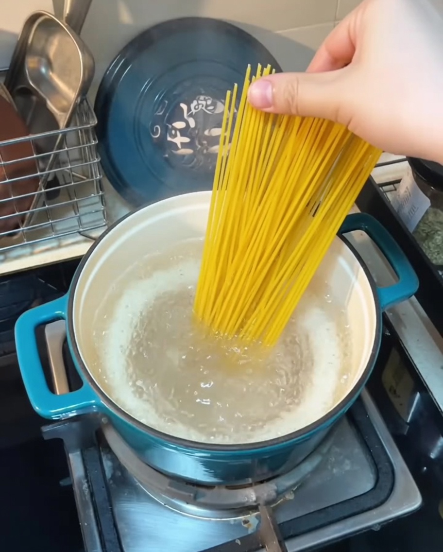 Nitki spaghetti wkładane do garnka z wrzącą wodą.