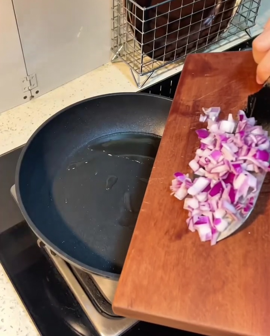 Pokrojony boczek i cebula smażące się w rozpuszczonym maśle na patelni.