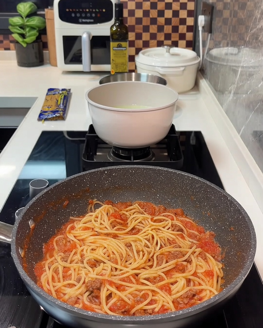 Patelnia pełna spaghetti z sosem mięsnym i kilkoma plastrami żółtego sera ułożonymi na wierzchu.