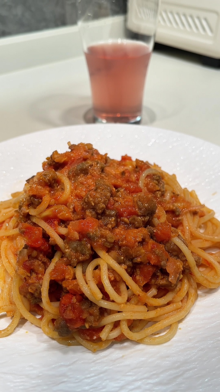 Apetyczna porcja spaghetti z bogatym sosem mięsno-pomidorowym i roztopionym serem.