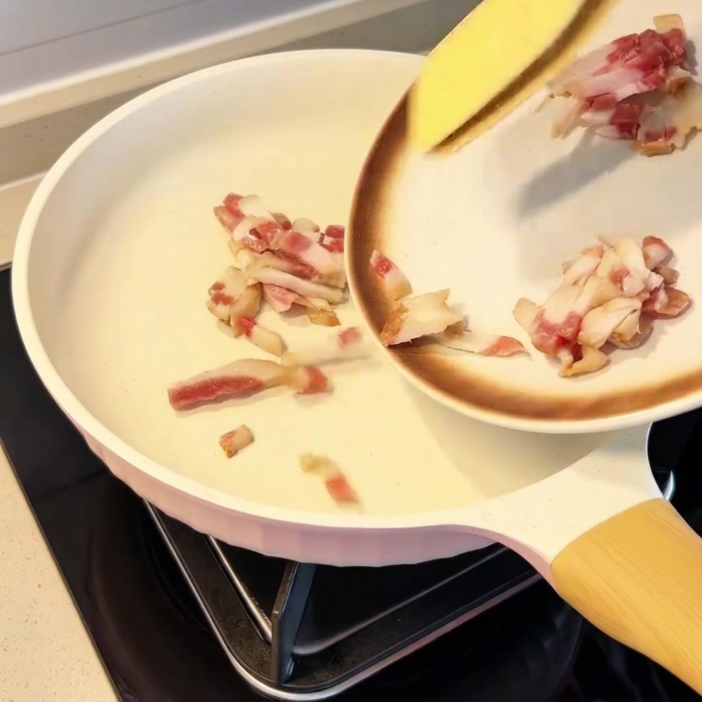 Kawałki guanciale równomiernie rozłożone na zimnej patelni.