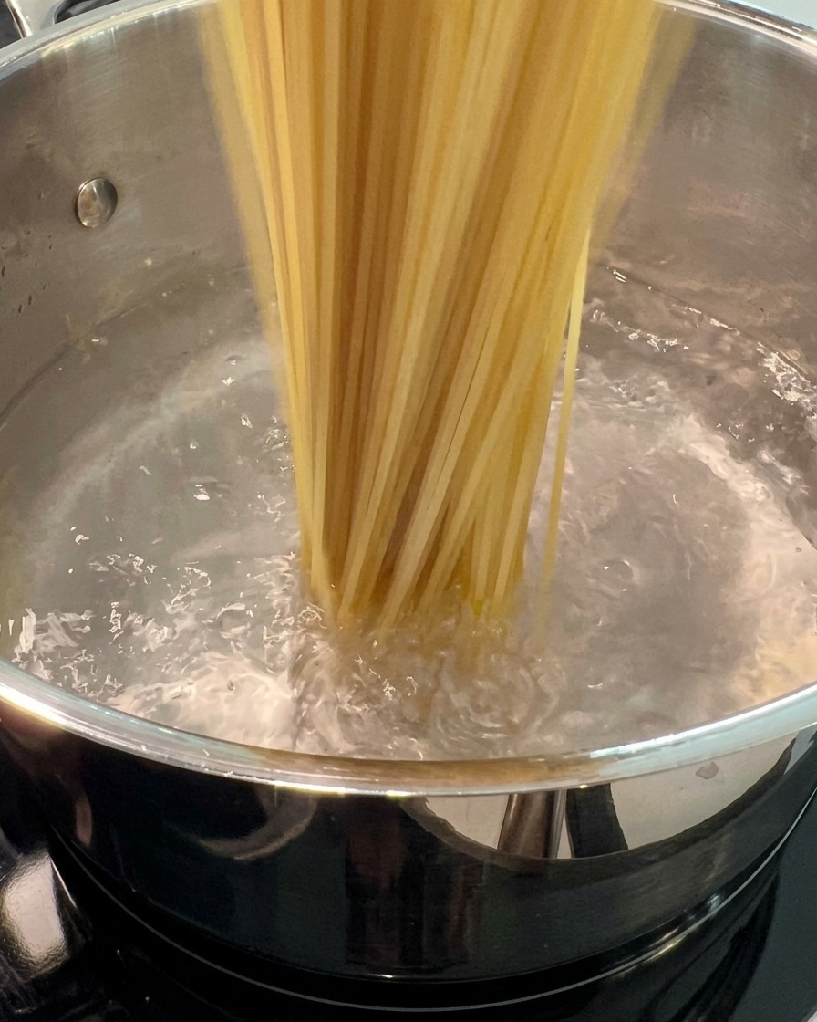 Surowy makaron spaghetti zanurzony w dużym garnku z wrzącą wodą.