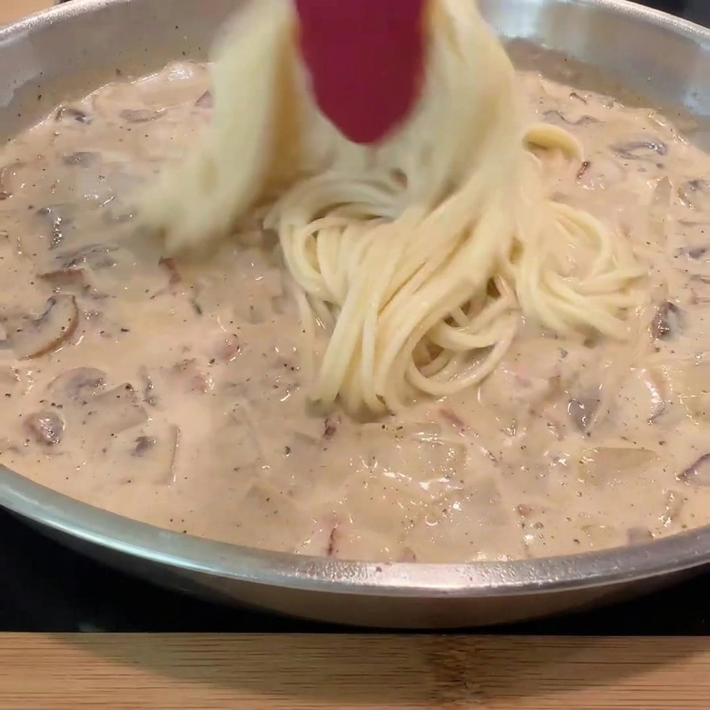 Ugotowane spaghetti dodawane do patelni z kremowym sosem.