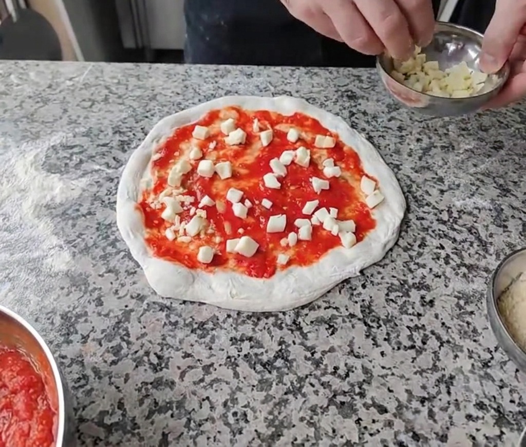 Posypywanie pokrojonych serów na sos pomidorowy.