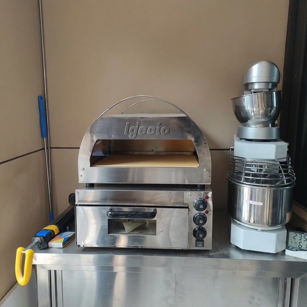 Surowa pizza wsuwana do gorącego pieca z widocznymi płomieniami.