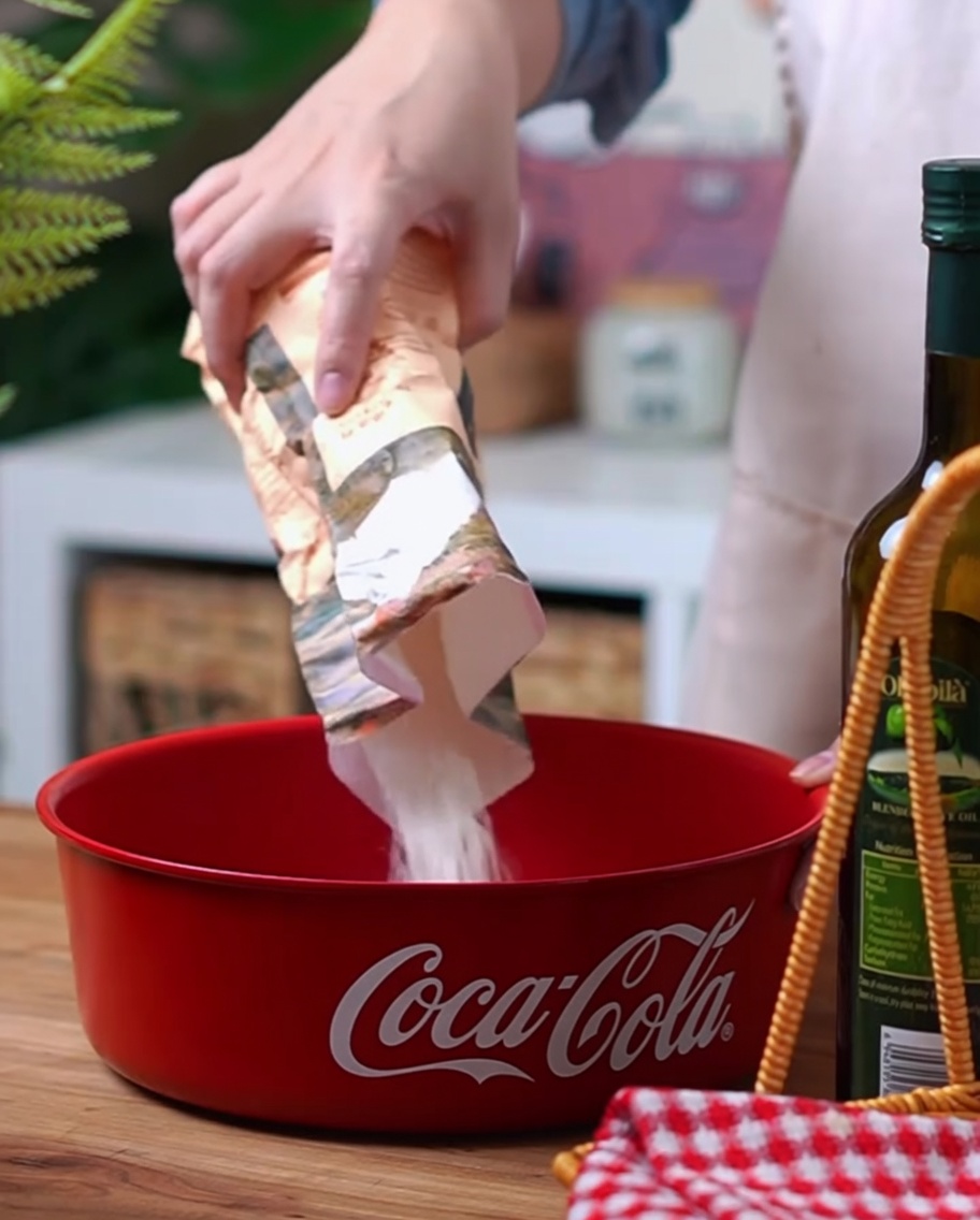 Zbliżenie na mąkę wysokobiałkową, drożdże i sól wsypywane do czerwonej miski Coca-Cola.