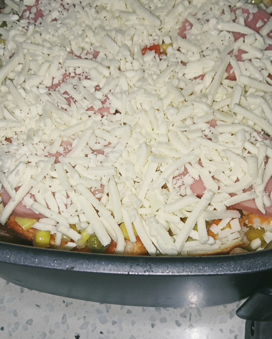 Zbliżenie na obfitą warstwę startego sera przykrywającą szynkę i warzywa w koszu frytkownicy.