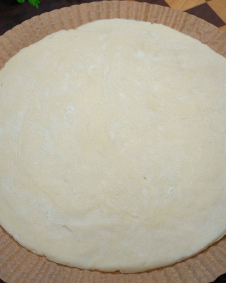 Zbliżenie dłoni formujących brzegi surowego, okrągłego placka cebulowego na papierze do pieczenia w celu uformowania brzegów pizzy.