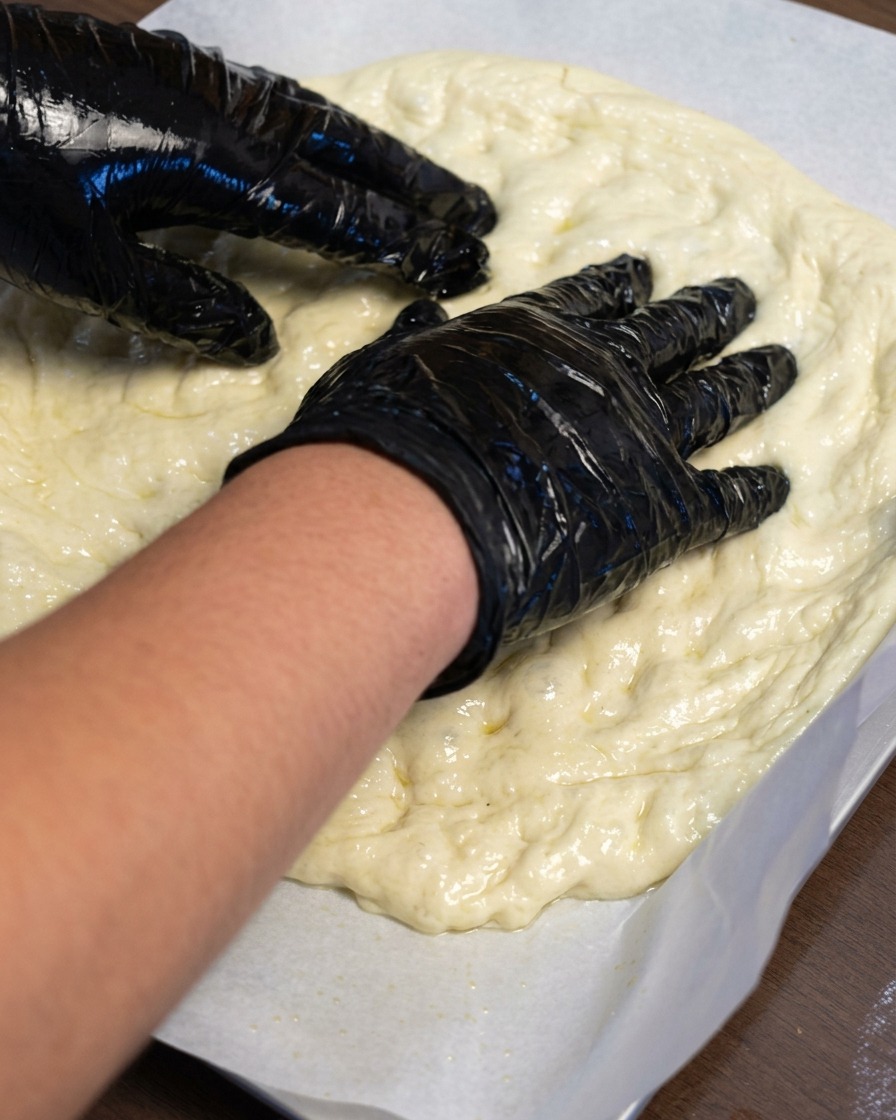 Dłonie rozciągające ciasto na pizzę na papierze do pieczenia.