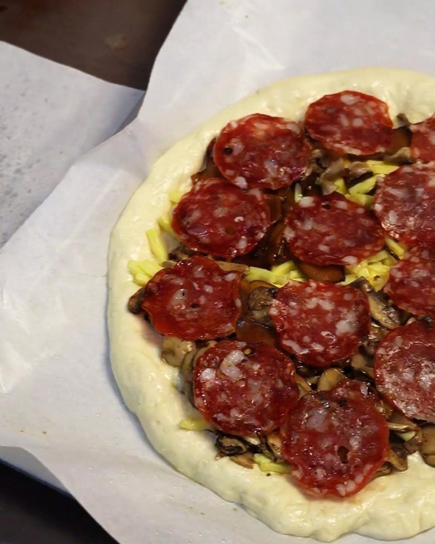 Zbliżenie na dłoń kładącą plasterki pepperoni na warstwę grzybów i sera.