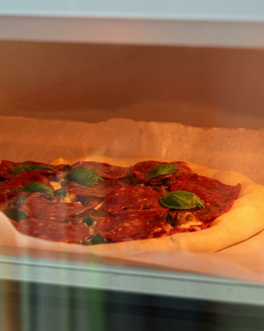 Surowa pizza z serem, grzybami i pepperoni wkładana do gorącego piekarnika.