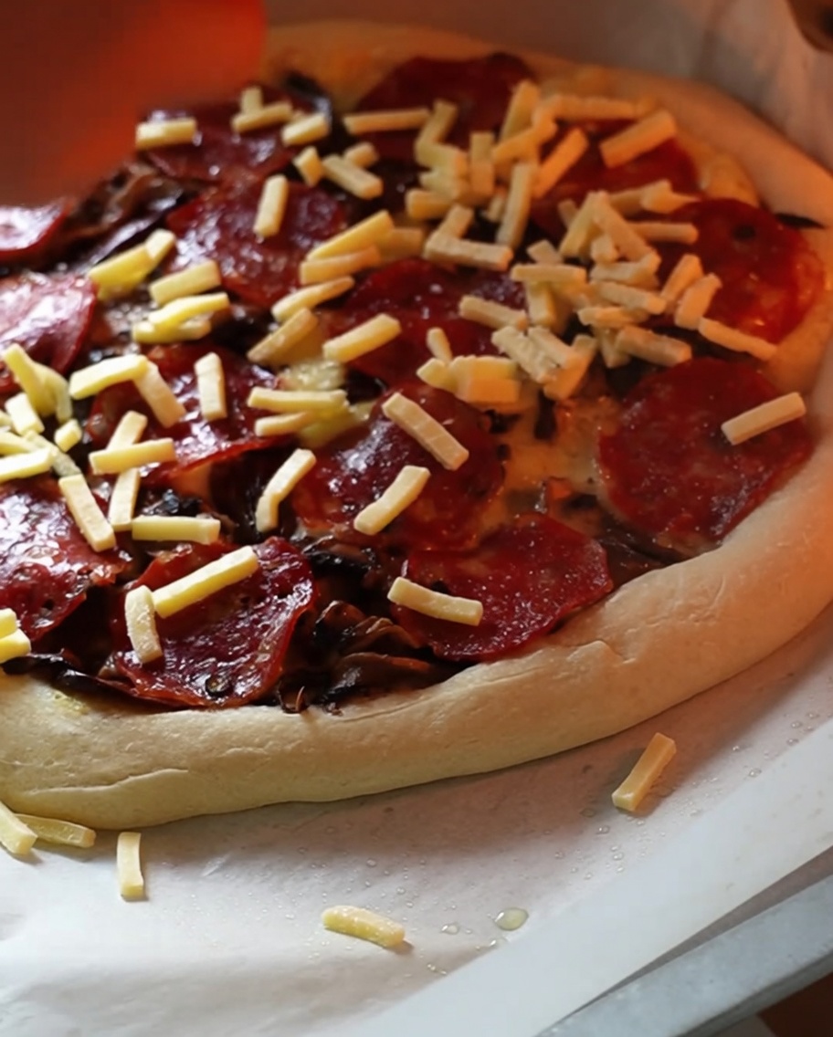 Podpieczona pizza w piekarniku posypywana dodatkową warstwą sera.
