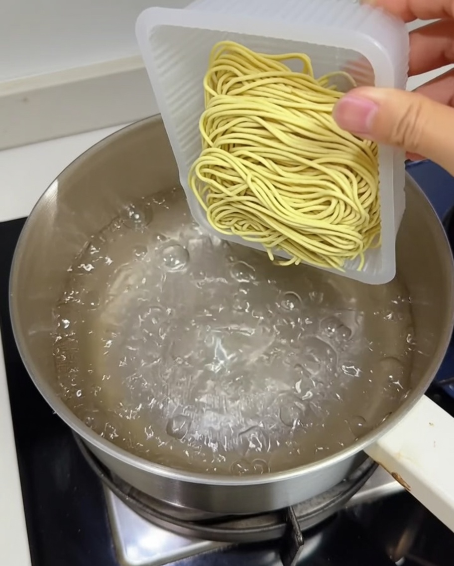 Blok świeżego żółtego makaronu ramen wkładany do garnka z wrzącą wodą.