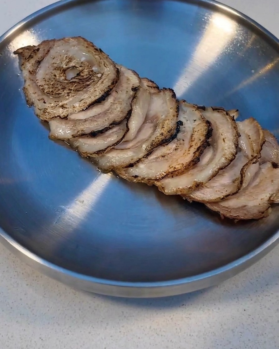 Plastry Char Siu przypiekane palnikiem kuchennym na metalowej tacy.