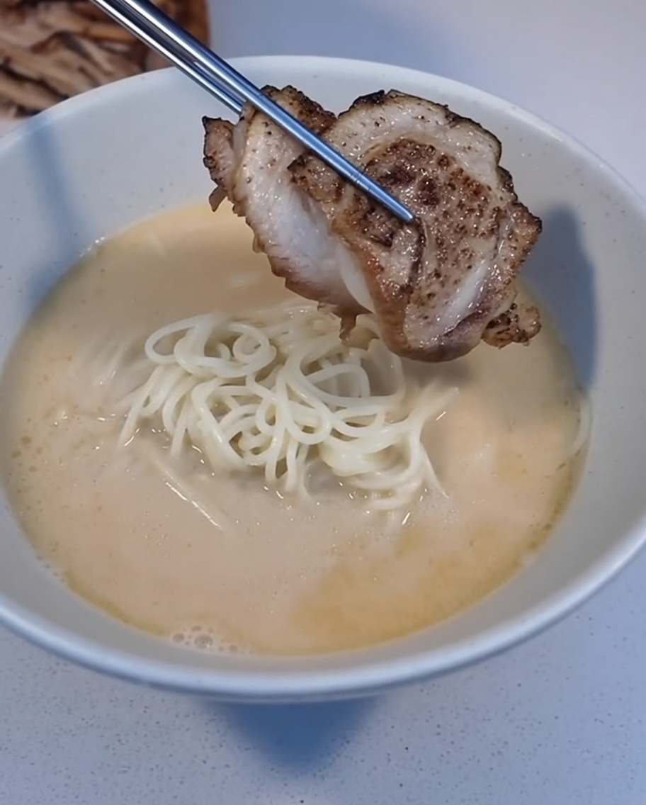Plaster przypieczonego Char Siu kładziony pęsetą na ramen w misce.