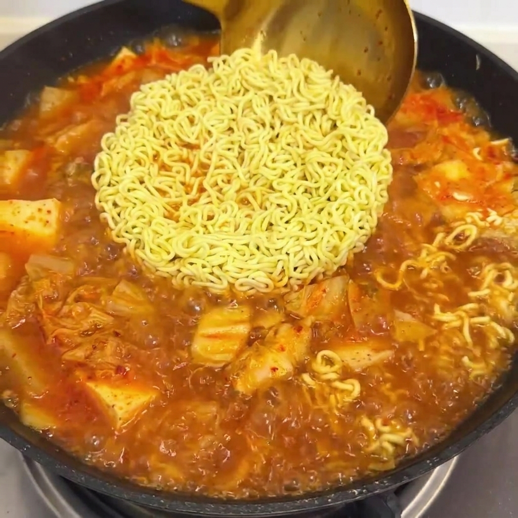 Czerwony sos wlewany na patelnię z gotującym się makaronem i bulionem z kimchi.