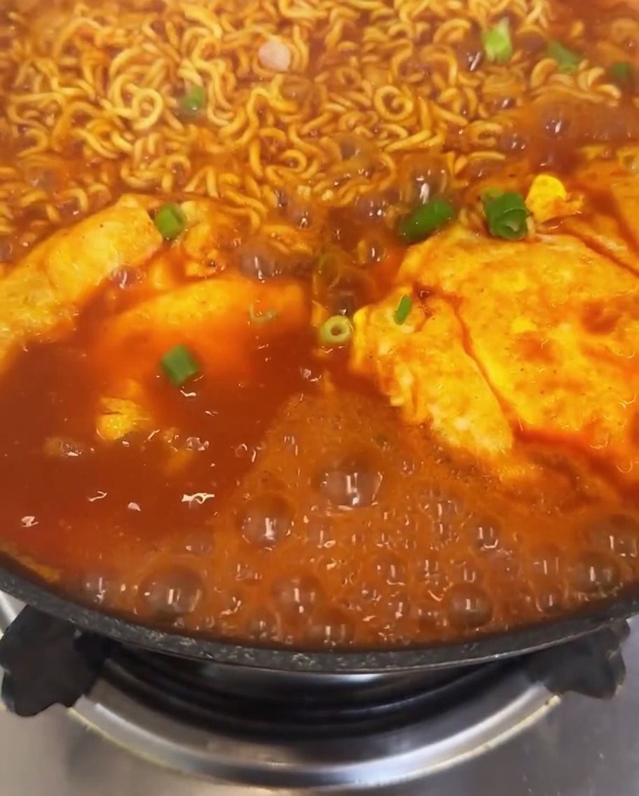 Zbliżenie na garnek ramenu z kimchi z posypanym świeżym szczypiorem i jasnoczerwonymi plastrami chili na bulgoczącym bulionie.