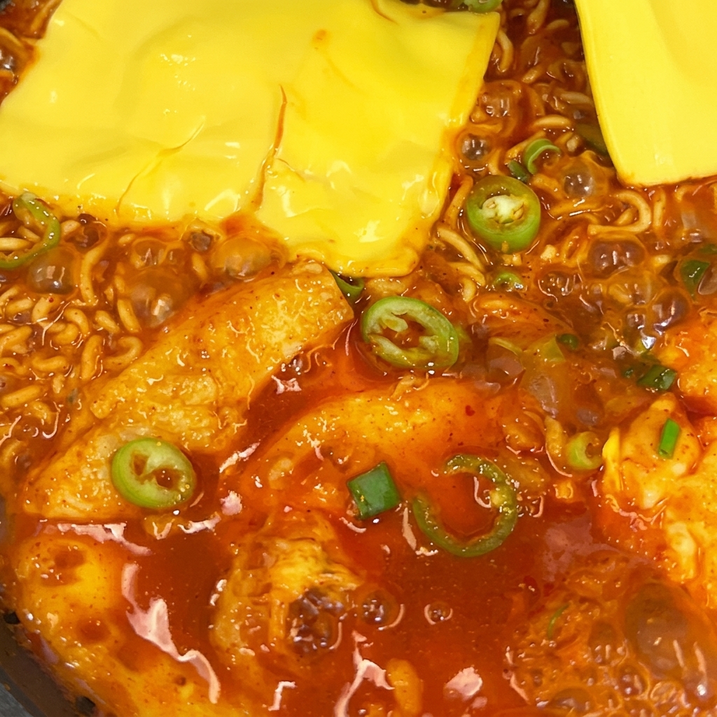 Dwa plastry żółtego sera topiące się na pikantnym makaronie ramen na patelni.