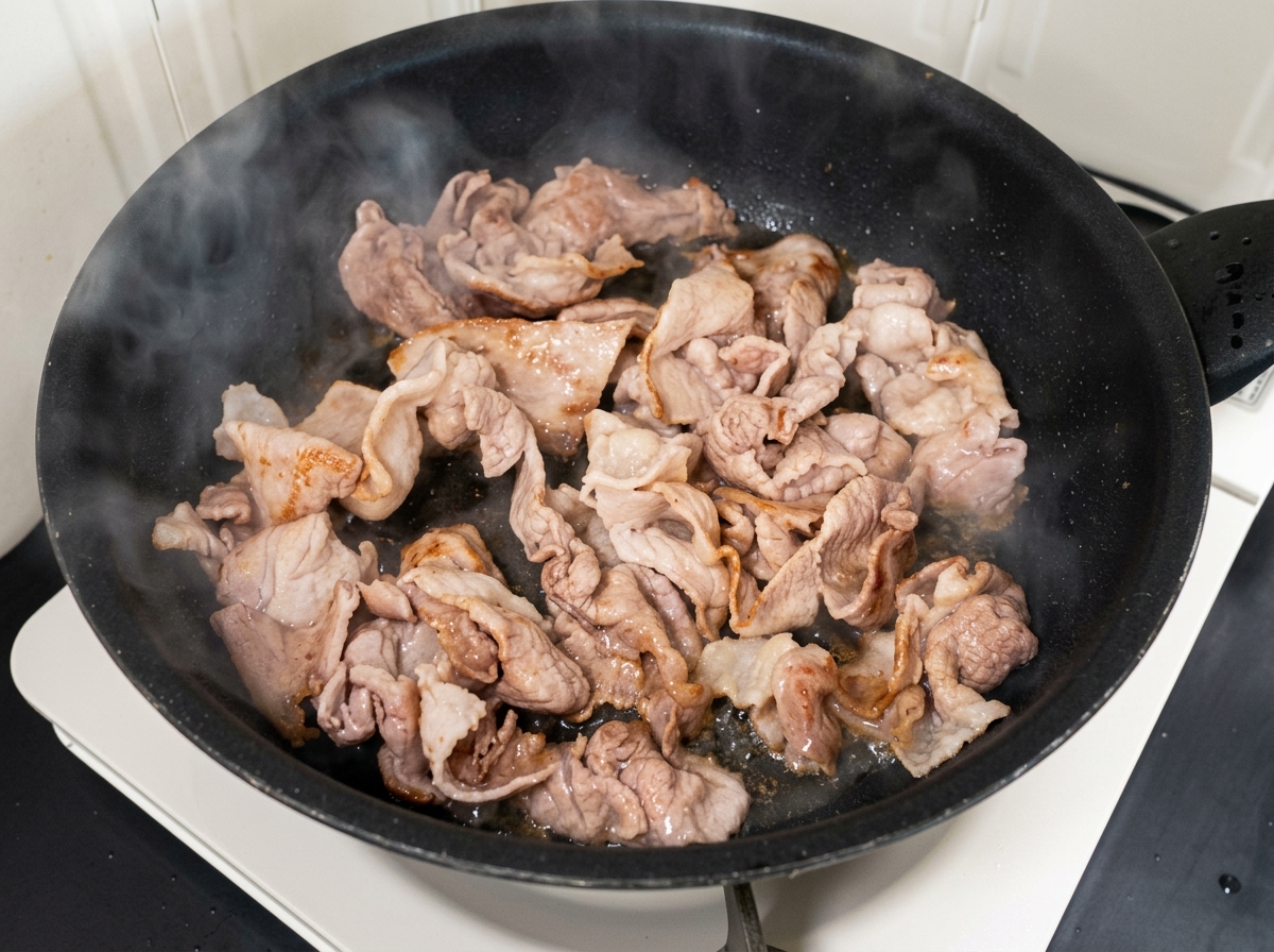 Posiekane kimchi i cukier wymieszane z usmażoną wieprzowiną na patelni.