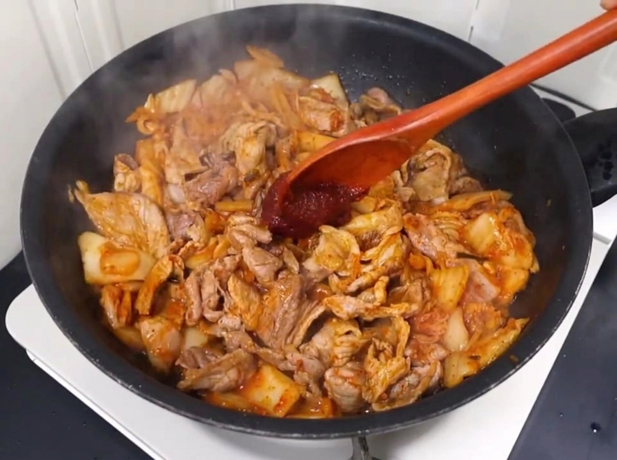 Pasta chili i płatki chili dodawane do smażącej się wieprzowiny z kimchi.