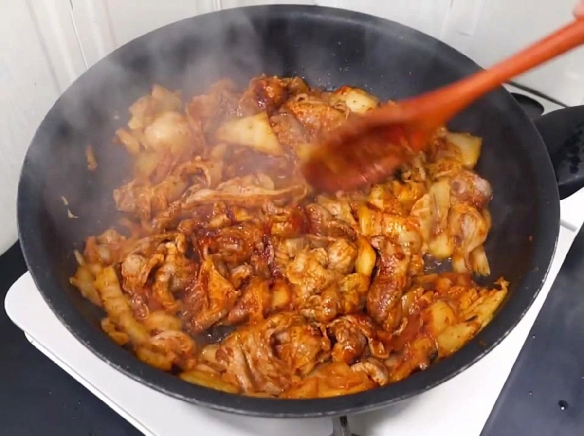 Woda wlewana na patelnię z podsmażoną wieprzowiną i kimchi.