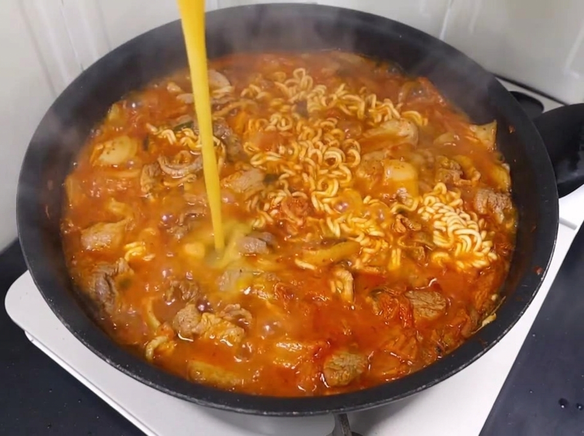 Roztrzepane jajko wlewane do bulgoczącego bulionu z makaronem, wieprzowiną i kimchi.