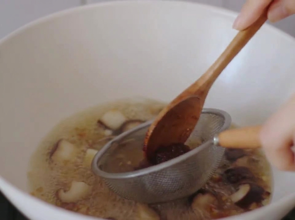 Pasta miso rozpuszczana w gotującym się bulionie przy użyciu małego metalowego sitka i drewnianej łyżki.