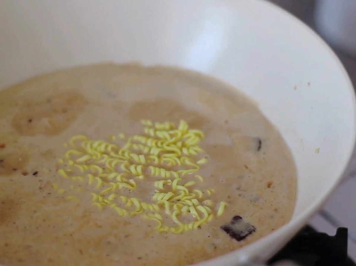 Makaron instant i plasterki ciastka rybnego narutomaki gotujące się w kremowym bulionie.