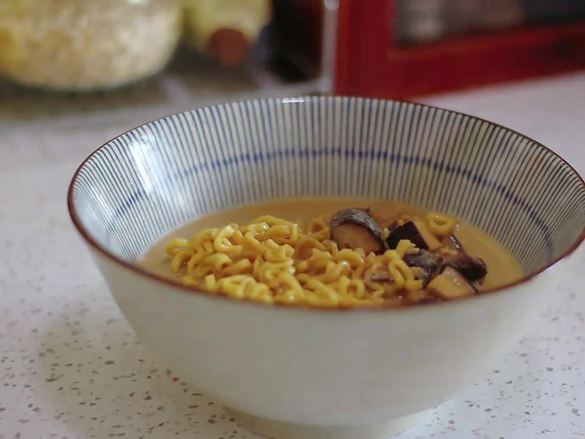 Makaron ramen i kremowy bulion nakładane chochlą do miski w paski.