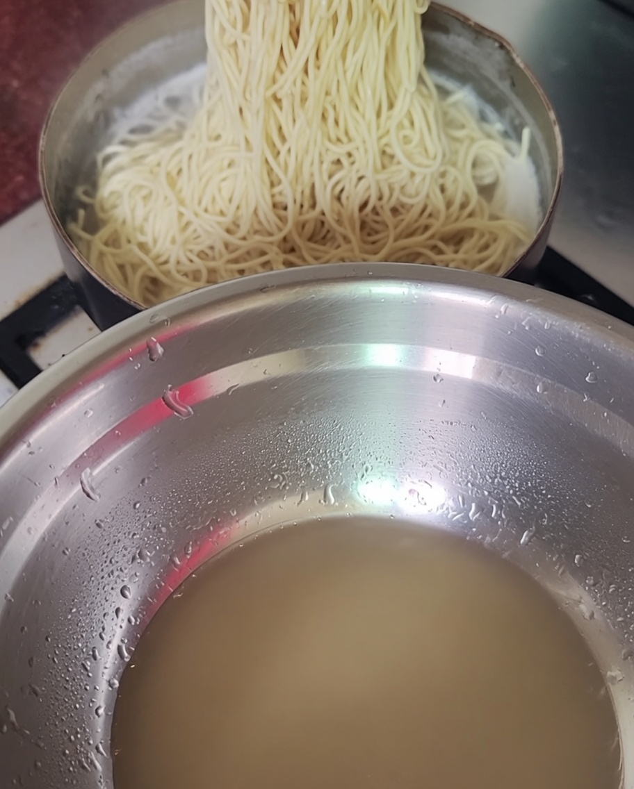 Ugotowany makaron wyjmowany z garnka za pomocą pałeczek.