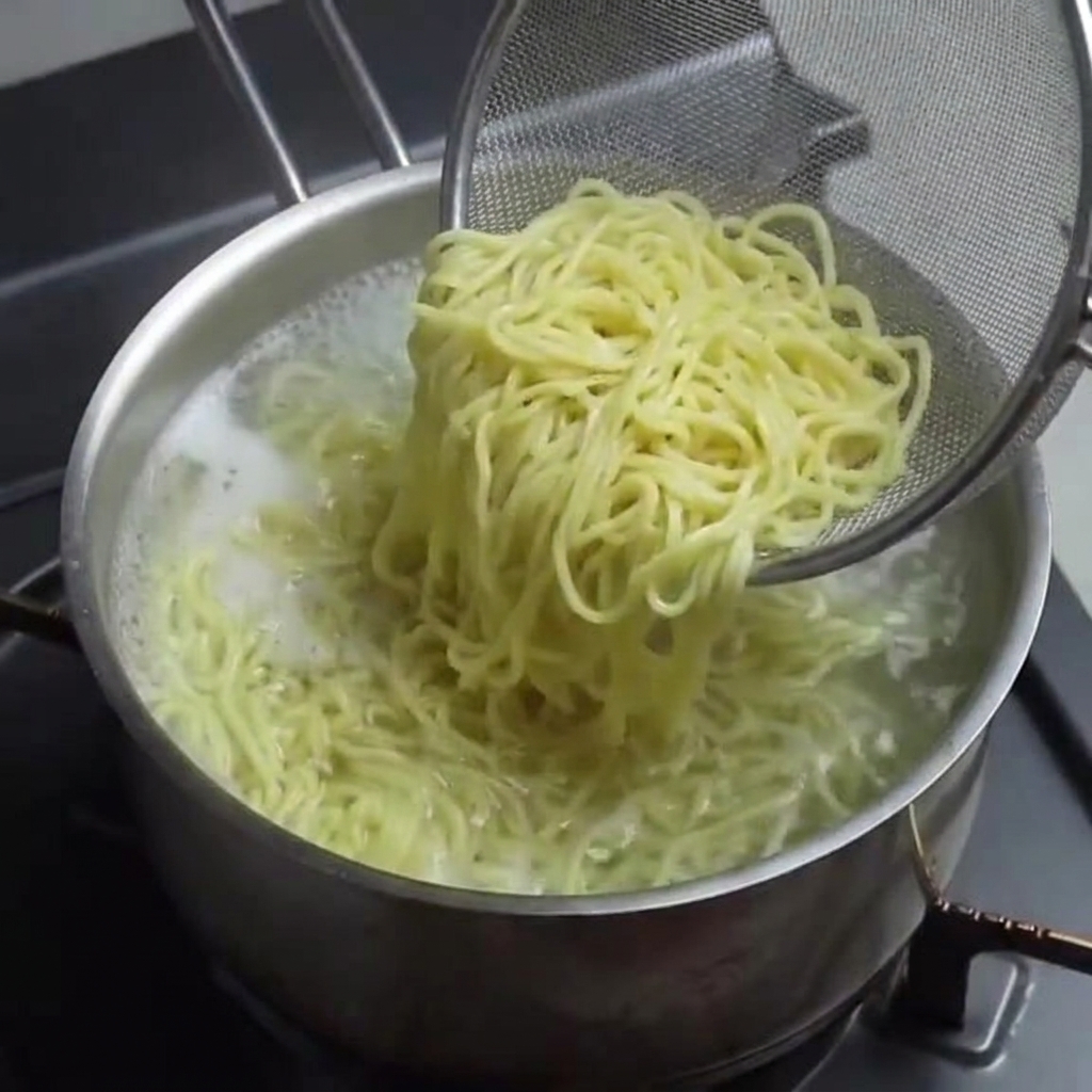 Ugotowany makaron ramen wyjmowany z garnka za pomocą drucianego sitka.