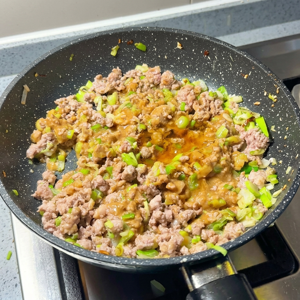 Patelnia z mięsem, miso i szczypiorkiem przyprawiana proszkiem chili i cukrem.