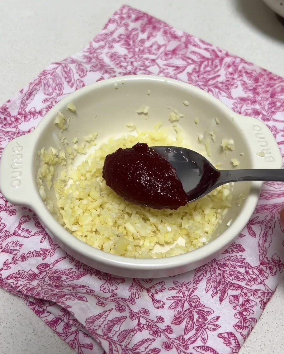 Mała miseczka z posiekanym czosnkiem i łyżką koreańskiej pasty chili mieszanymi z odrobiną wywaru.
