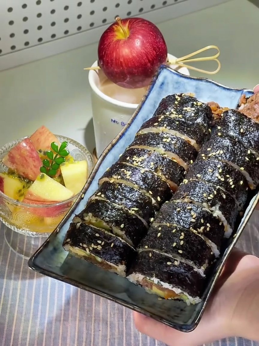 Pokrojone koreańskie gimbap posypane sezamem, podane z miseczką jabłek marynowanych w marakui.