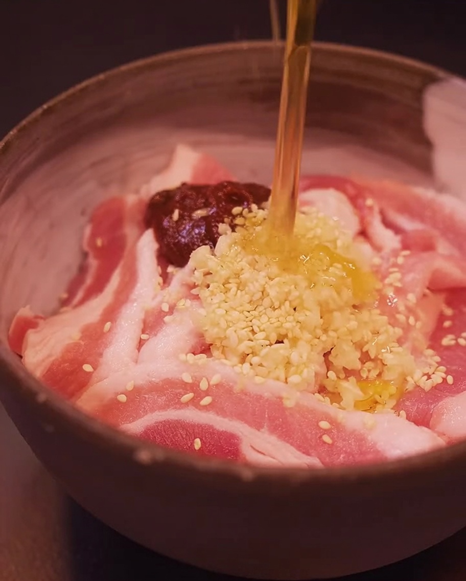 Plastry boczku w misce przyprawiane pastą gochujang, czosnkiem, sezamem i olejem sezamowym.