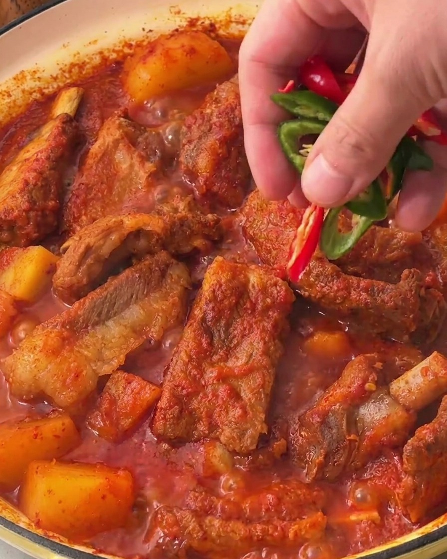 Dłoń posypująca świeże plasterki zielonej i czerwonej papryczki chili na powierzchnię gotowych żeberek.