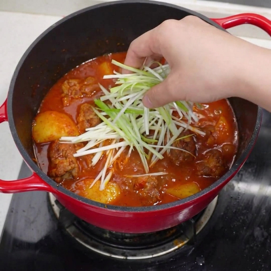 Gotowy garnek duszonych żeberek wieprzowych, posypany zieloną cebulką, plasterkami czerwonego chili i czarnym pieprzem.