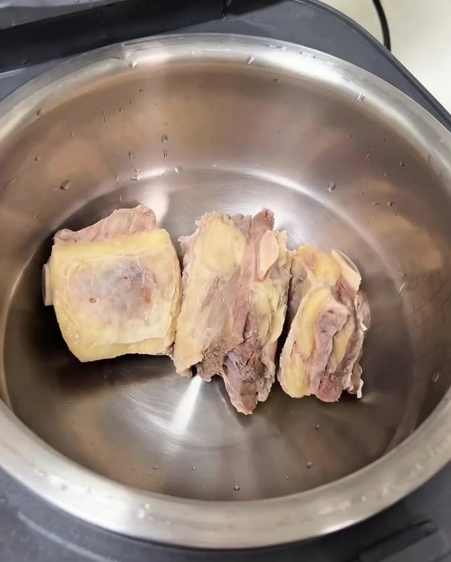 Wewnętrzny garnek urządzenia do gotowania ryżu zawierający oczyszczone żeberka wołowe i różne aromaty.