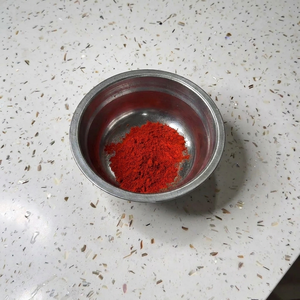 Mała metalowa miseczka zawierająca kopiec czerwonego chili w proszku i białego cukru na granitowym blacie.