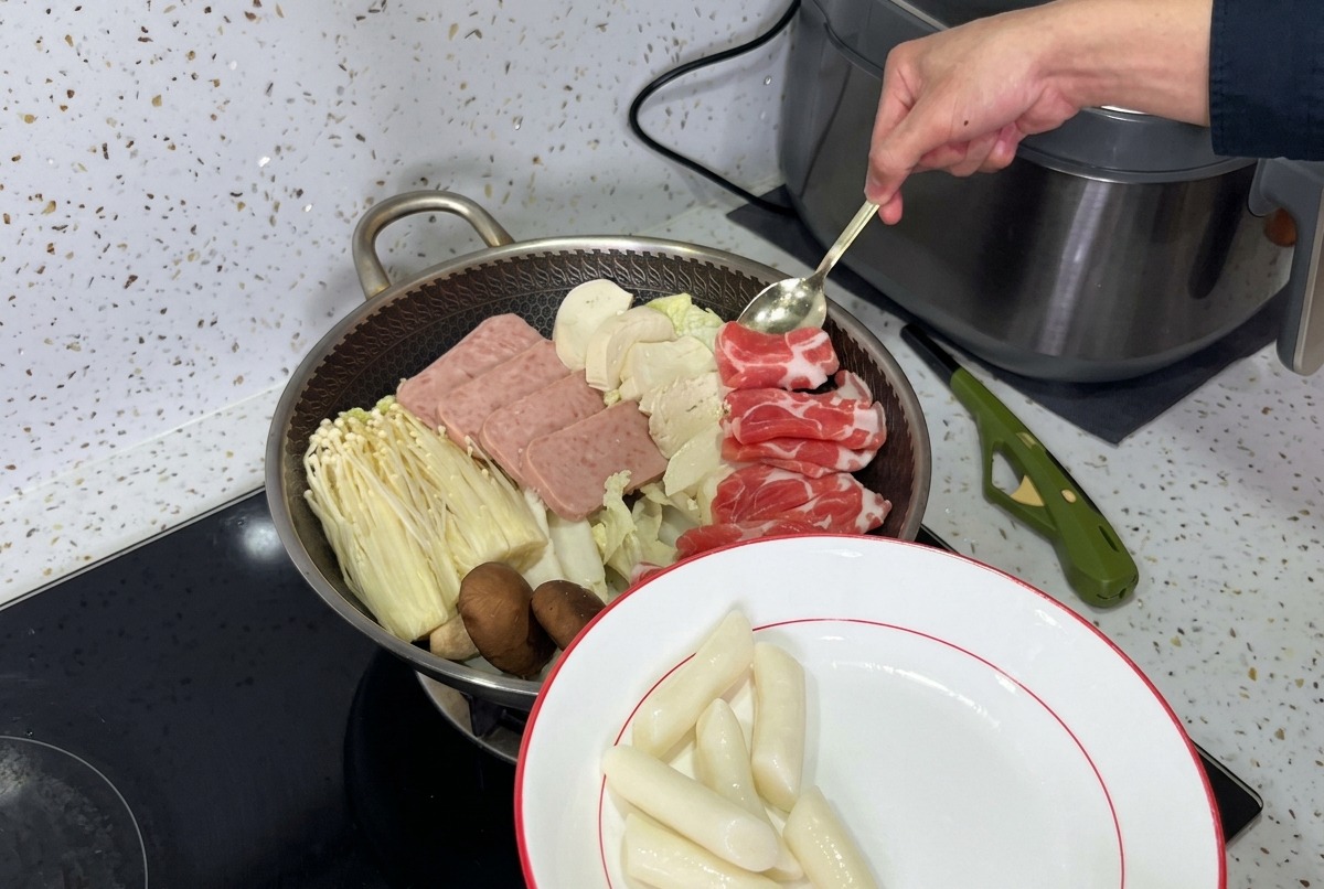 Pięknie ułożony garnek koreańskiego gulaszu armijnego z warstwami mielonki, grzybów, tofu i świeżego kimchi gotowego na bulion.