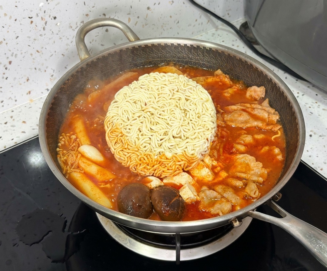 Kostka makaronu ramen gotująca się w centrum tętniącego życiem, bulgoczącego koreańskiego gulaszu armijnego.
