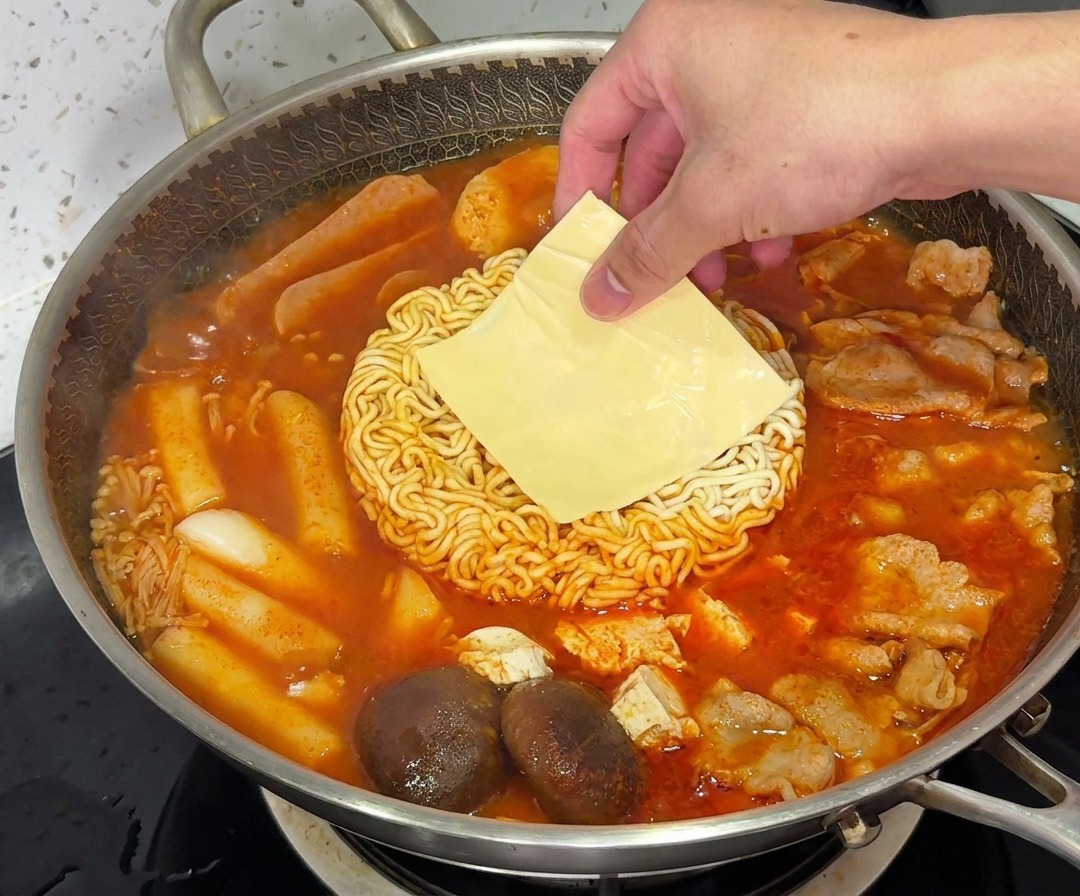 Plasterek żółtego sera topiący się na makaronie ramen w parującym garnku Budae Jjigae.