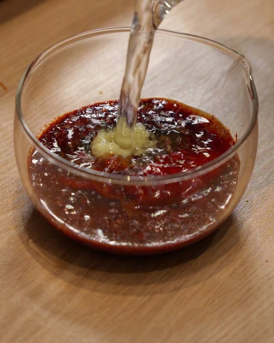 Woda wlewana do szklanej miski z proszkiem chili i przyprawami.