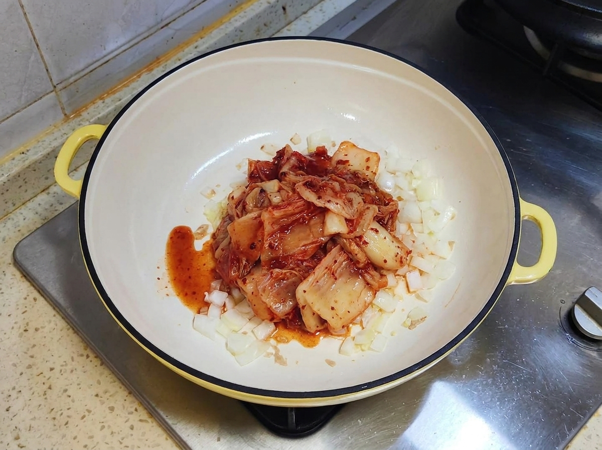 Porcja czerwonego sfermentowanego kimchi spoczywająca na podsmażonej cebuli na białej patelni.