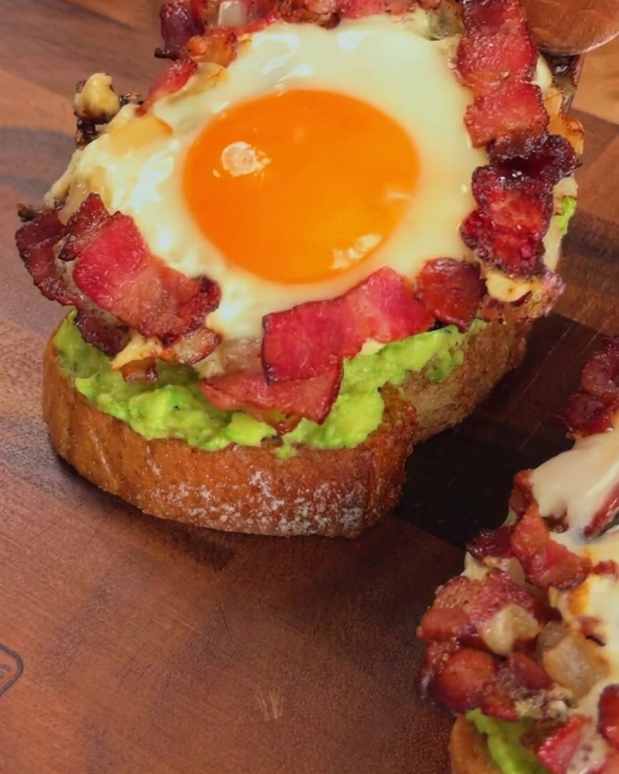 Ugotowany pierścień z boczku i jajka nakładany na tost z awokado za pomocą drewnianej łopatki.